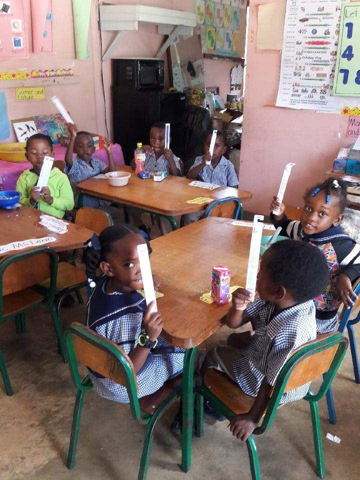 Young students seated at classroom tables holding up donated supplies during a Simunye outreach trip.