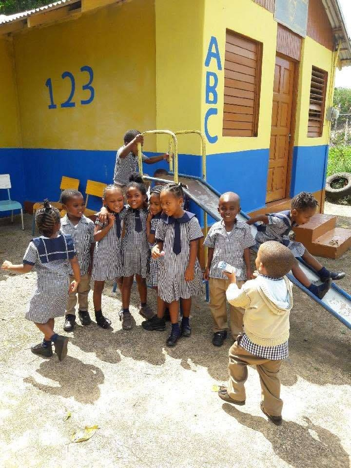 Children in school uniforms playing outside a colorful building during a Simunye outreach trip.